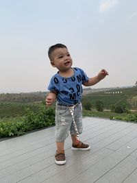 Portrait of cute boy standing on field against sky