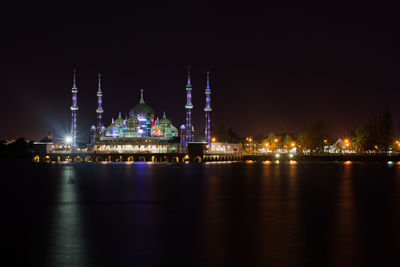 Illuminated mosque by river against sky at night