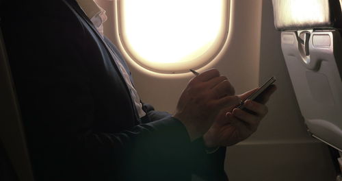 Midsection of man using mobile phone in airplane