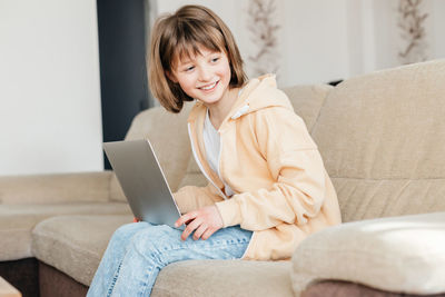 The schoolgirl sits on the couch and writes in a laptop. the child is learning using gadgets at home