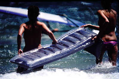 Rear view of female friends carrying pool raft in sea