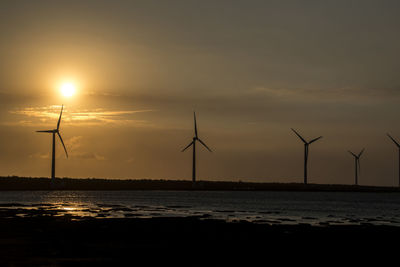 Silhouette wind turbine against sky during sunset