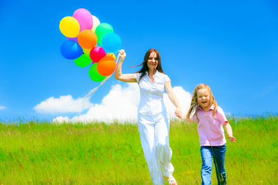 Full length portrait of happy friends standing on field against blue sky