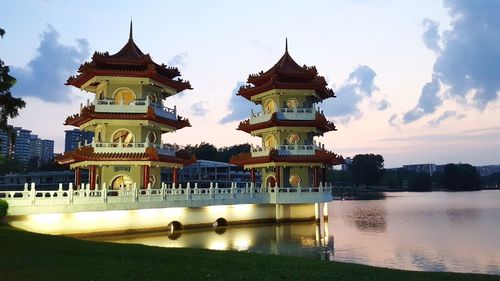 Building by lake against sky during sunset