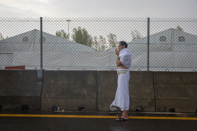 Rear view of boy standing by chainlink fence against sky