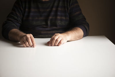 Unrecognizable man in a familiar position sitting at a white empty table, focus on his hands