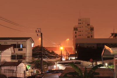 Illuminated street amidst buildings against sky at sunset