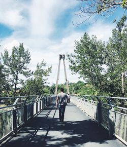 Man walking on footbridge against trees