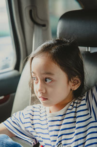 Young little girl enjoying the trip in back seat looking out the window of the car