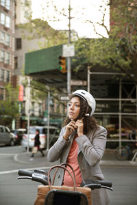 Businesswoman wearing helmet while standing by bicycle on street