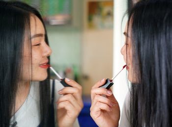 Close-up of woman applying lipstick while looking at mirror