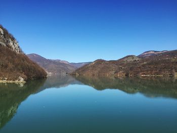 Scenic view of lake and mountains against clear blue sky