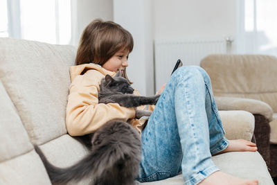 Social media. a schoolgirl girl sits on the couch hugging a cat and with a phone in her hands 
