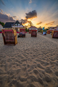 Hooded chairs on beach against sky during sunset