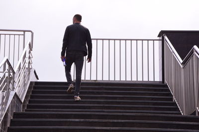 Rear view of man walking on staircase against sky