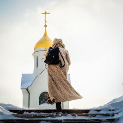 Rear view of woman walking on steps at church against sky during winter