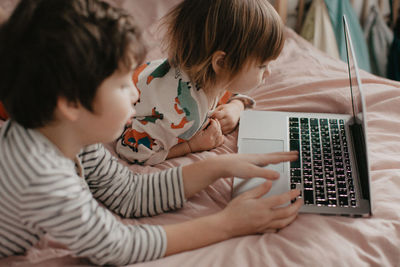 Little brother and sister lie in the bedroom on the bed and look at the laptop. high quality photo