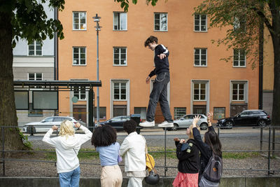 Male teenager balancing on railing while friends cheering on footpath