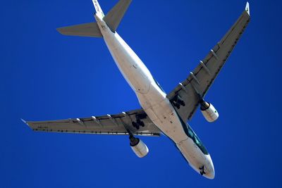 Low angle view of airplane flying against clear blue sky