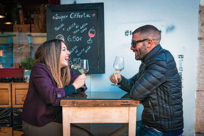 Couple holding wineglasses on table talking while sitting at outdoor cafe