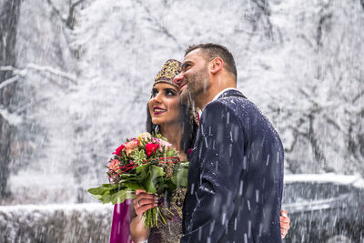 Bride holding bouquet while standing with groom on snow covered footpath