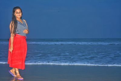 Full length of young woman standing on beach against sky at dusk