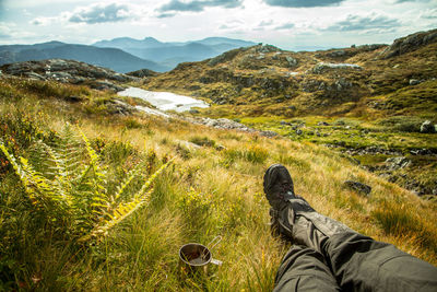 Low section of person relaxing on field against mountain