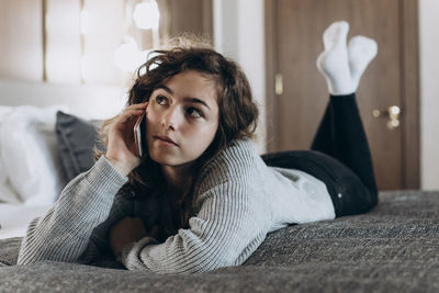 Happy smiling teenager girl talking by phone lying on her bed