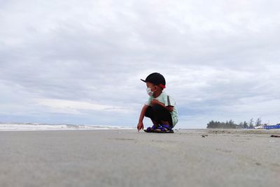 Rear view of boy on beach against sky