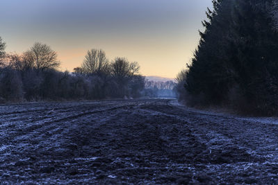 Surface level of snowy field against sky during sunset