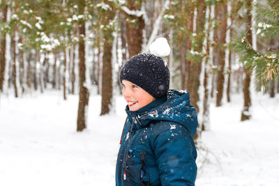 Smiling child boy in winter forest in snowstorm with snowball on head. funny kid on snowy winter 