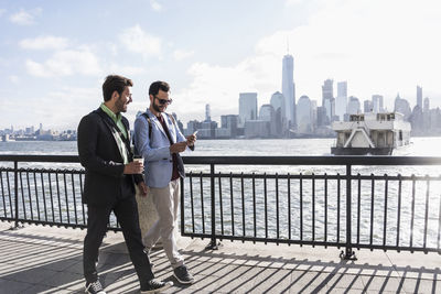 Usa, two businessmen walking at new jersey waterfront with view to manhattan