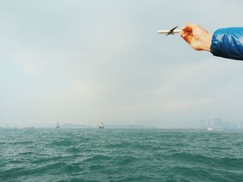 Optical illusion of person holding airplane flying over sea