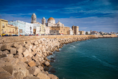 View of buildings by sea against blue sky