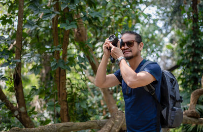 Young man photographing through camera in forest