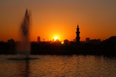 Silhouette city by river against sky during sunset