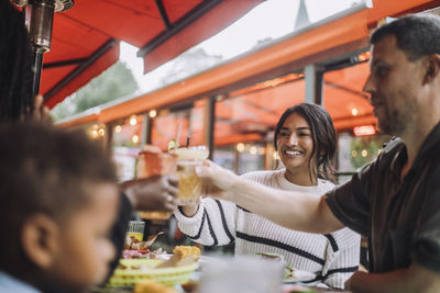 Smiling woman toasting drinks with family while celebrating at restaurant