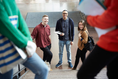 Smiling friends looking at female university students on steps while standing in corridor