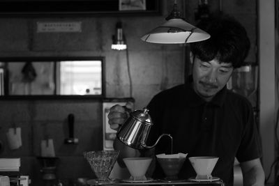 Mid adult man pouring coffee in cup on table at home