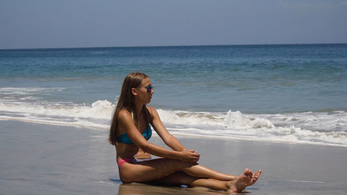 Girl in the sun glasses sits on a sandy beach among the waves and looks at the sea.