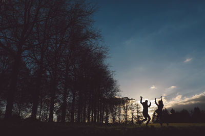 Silhouette women jumping over grass at les jardins d annevoie against sky