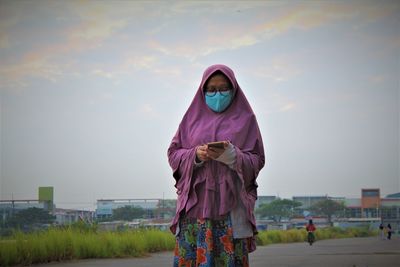 Woman using phone while standing against the sky