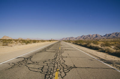 Empty road leading towards mountains against blue sky