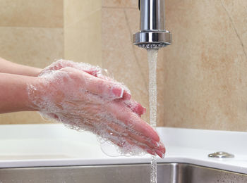 Close-up of hand touching water from faucet in bathroom