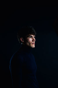 Portrait of young man standing against black background