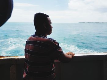 Rear view of man standing by sea against sky
