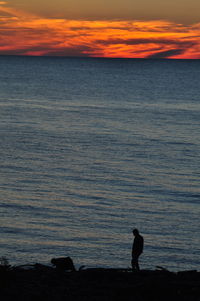 Silhouette man standing on beach against sky during sunset