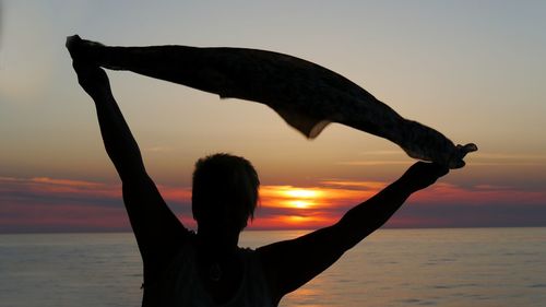 Silhouette woman holding scarf at beach against sky during sunset