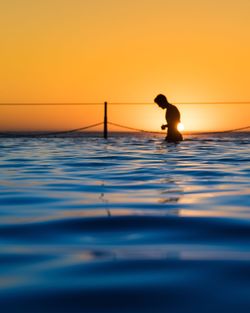 Silhouette man walking in sea against sky during sunset