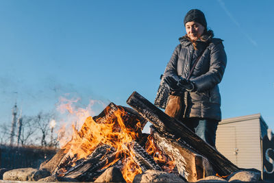 Low angle view of woman standing by bonfire against blue sky